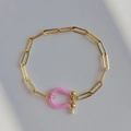 Detailed close-up of a gold chain bracelet featuring a pink enamel horseshoe buckle charm - Pink