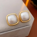 Detalle de pendientes cuadrados dorados con centro plateado sobre un cojín de joyería - Blanco
