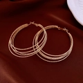 Macro detail of golden multi-layer hoop earrings on deep red velvet background - Gold