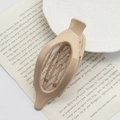 Beige oval cutout plastic hair claw clip on a book page for elegant styling - Glossy Skin