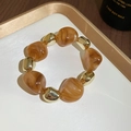 Detail of amber acrylic and gold beads bracelet on a white tray with wood background - Bracelet / Brown