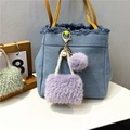 Close-up of purple faux fur mini bag keychain with pearl charm on denim background - Lavender