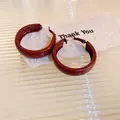 Detail view of retro wine red C-shaped hoop earrings on elegant textured background - Dark Red Wide Hoop