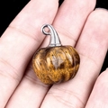 Tiger eye stone pumpkin pendant with silver bail held in hand against black background - Tiger's Eye