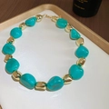 Detailed view of turquoise acrylic beads and gold metal beads on a display tray - Necklace / Green