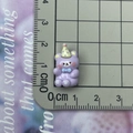 Dettaglio di un orsetto in resina viola in miniatura con cappello da festa e fiocco blu - Orso con cappello viola