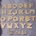 Flat lay of 26 golden metal A-Z alphabet charms with clear rhinestone inlays on grey fabric - Rhinestone Alphabet Set (DY147) / Set of 26 / Style 54 Large KC Gold