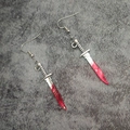 Macro shot of silver dagger earrings with red blood stains for Halloween theme decor - Cleaver
