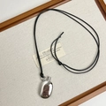 Detailed view of oval polished metal pebble pendant with black cord on a wooden tray - Silver Wine Jug