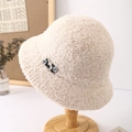 Close-up of beige lamb wool bucket hat with black patch detail on a wooden stand - Beige