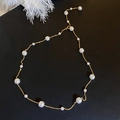 Elegante collar de cadena dorada con perlas blancas alternas sobre un fondo negro neutro - Oro Perla Artificial