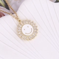 Dettaglio del ciondolo a girasole dorato con faccina, smalto bianco e zirconi lucenti - Bianco