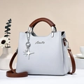 Detalle del bolso de piel gris claro con asas marrones y colgantes de metal plateado - Gris