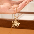 Detail of a gold sun pendant necklace held by hand over a wooden jewelry box - Golden Sun Face Necklace