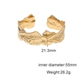 Dettaglio dell'ampio bracciale in acciaio dorato con texture martellata e bordi ondulati - Oro