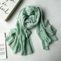 Light green modal scarf with fine texture and fringe trim on white wood surface - Bean Green