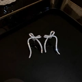 Boucles d'oreilles nœud argentées avec diamants scintillants sur un plateau noir - Argent Nœud Pavé