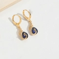 Detalle de pendientes de pavo real dorados con piedras azules y pequeños diamantes finos - Estilo Lágrima Azul Real