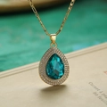 Macro-opname van een vergulde ketting met blauwgroene druppelkristal en pavé-stenen - Goud/Teal Zirkonia