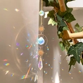 Detail of sun catcher crystals casting rainbow light on white wall with gold metal chain - B4