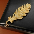 Detalle del broche de pluma dorada con cristales y colgante de la letra F - Dorado