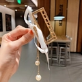 Gold hollow metal hair claw with white ribbon bow and pearl tassel pendant held in hand - Pearl Pendant Square With Ribbon / Gold
