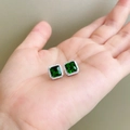 Detailed view of emerald green square stud earrings with halo diamonds on hand - Square Nano Green Zirconia Studs