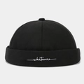 Front view detail of a stylish black brimless docker hat with white embroidered text - Adjustable / Black