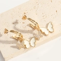 Detail of golden bow earring with white enamel wings and sparkling zircon on a stone - White