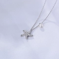 Detail der silbernen Seestern-Kette mit glänzenden Diamanten und weißer Perle auf Stoff - 925er Silber / Weiß