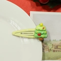 Close-up of a green resin Christmas tree hair clip with red bows on a ceramic plate - Beige Christmas Tree Hair Clip