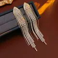 Elegantes pendientes largos de borla dorada con pedrería blanca sobre caja de joyas - Borla de Oro