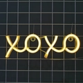 XOXO LED neon sign in warm yellow light hanging on a black grid for wall decoration - Warm White