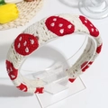 Cream crochet headband with red mushroom embroidery displayed on a clear stand - Strawberry Thin Style