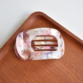Detailed view of pink marble acetate hair claw clip with cutout oval design on wood tray - Round Claw / Purple Red Floral