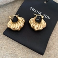 Detail of gold shell-shaped twist hoop earrings on a black card with beige plush background - Gold