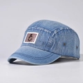 Detail van lichtblauwe gewassen denim pet met bruine lederen patch en metalen ringgesp - Denim Blauw
