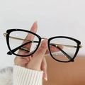 Occhiali cat-eye con montatura nera e stanghette dorate tenuti in mano - Anti-Luce Blu Trasparente / Blu Trasparente Oro