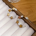 Dettaglio macro di orecchini a C con inserti metallici e perle su velluto beige - Stile Pietra Argento e Caffè / Argento-Caffè