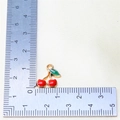 Macro shot of a red cherry enamel charm with gold alloy frame next to a measuring ruler - Style 7