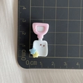 Macro detail of a 2.5cm resin shovel charm with smiley face on a centimeter scale pad - Pink and White Shovel