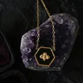 Macro shot of hexagonal honeybee pendant with black enamel on purple crystal cluster - Gold Black Bee / Black