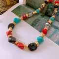 Dettaglio di collana vintage con perle di corallo rosso e turchese su un libro d'arte - Collana di perline irregolari multicolore