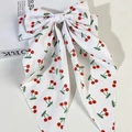 Detail of white bow hair clip with cherry print and long ribbons on a magazine - White Background Red Cherry Print / White
