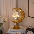 Detail einer warmen LED-Lichterkette in einer goldenen Mondsichel-Lampe auf dem Nachttisch - Mondlampe Hängestern Stil / Warmweiß
