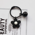 Close-up of black flower charm and metal bell on key ring with minimalist card detail - Black