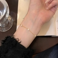 Elegant gold clover bracelet with white zircons worn on wrist over a vintage book - 925 Silver / 18K Gold