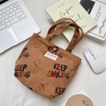 Detail van corduroy draagtas met KEEP SMILING-print en vintage metalen drukknopsluiting - Bruin