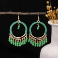 Close-up of bohemian round hoop earrings with green tassels hanging on a wood branch - Green