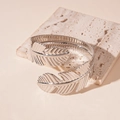Detailed view of silver feather cuff bracelet with hollow design on stone surface - Silver